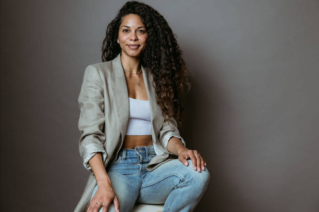 Soulful strategy studio portrait—woman seated in blazer and jeans, embodying calm clarity for aligned wealth.